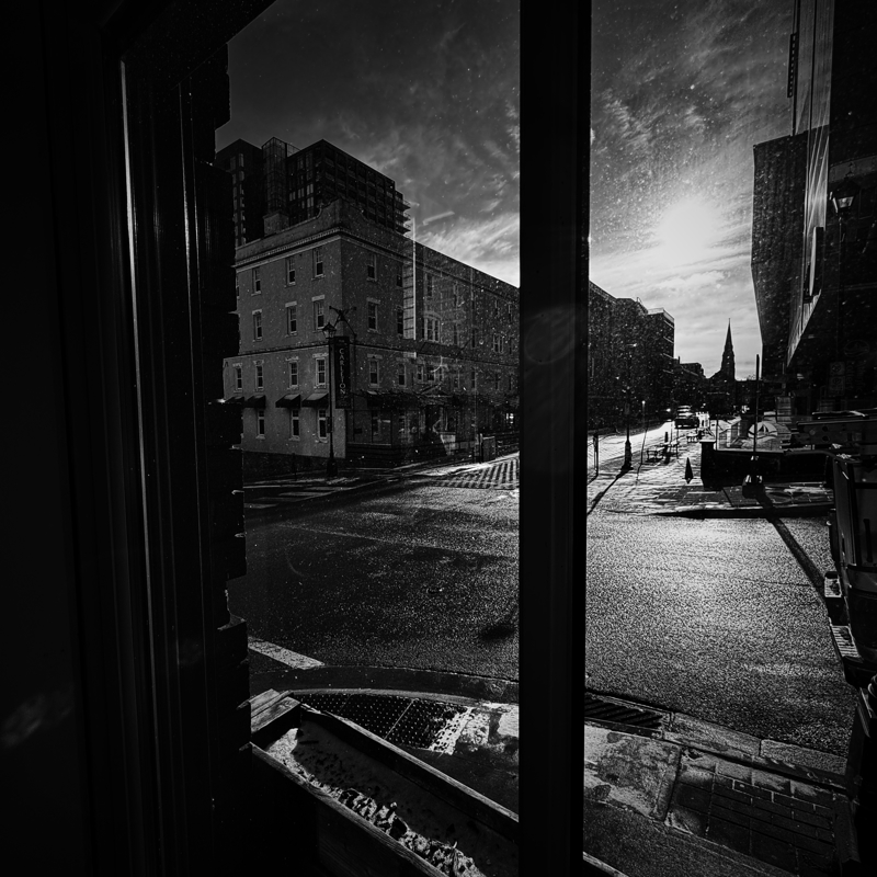 Wet pavement at an intersection shines in the bright sunlight seen through a large window