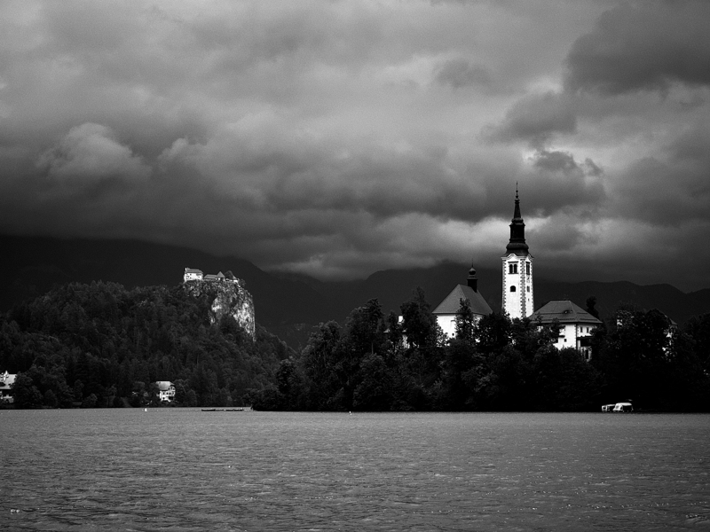 A church sits atop an island in the middle of a lake with a castle overlooking from atop a cliff