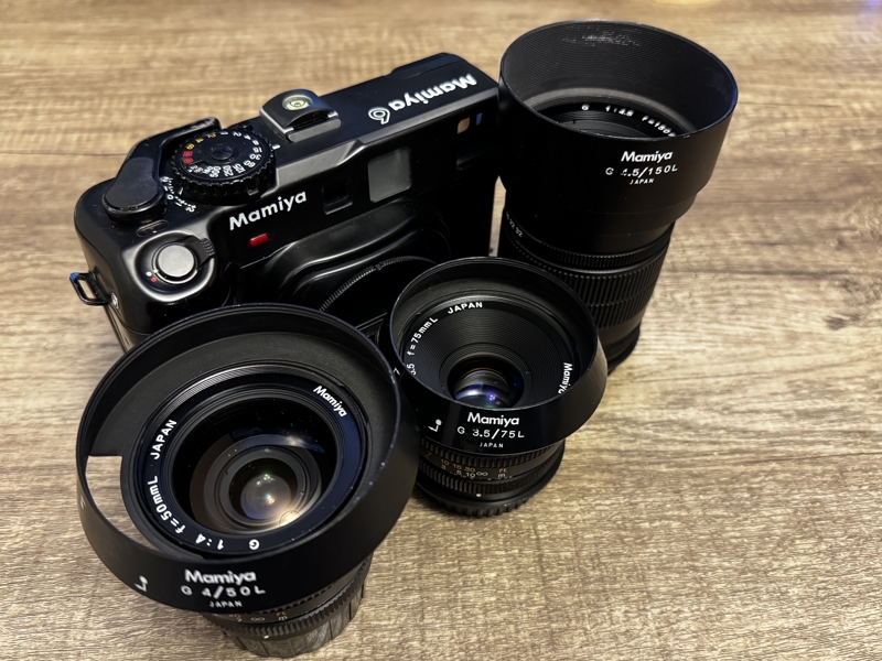 Back from the camera hospital A large black camera sites next to three matching black lenses on a dark grey coloured table