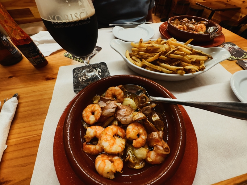 Checked in: Arco Da Velha A dish of prawns and garlic in oil in a dark brown dish with a glass of dark beer to the side