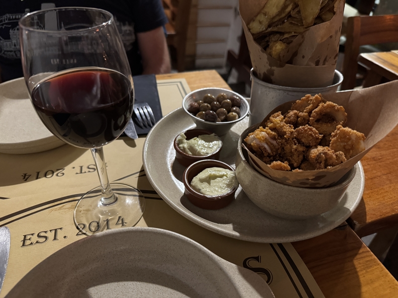 Checked in: Tasca Das Tias A selection of mixed snacks on a few plates in a darkened restaurant with a glass of wine beside