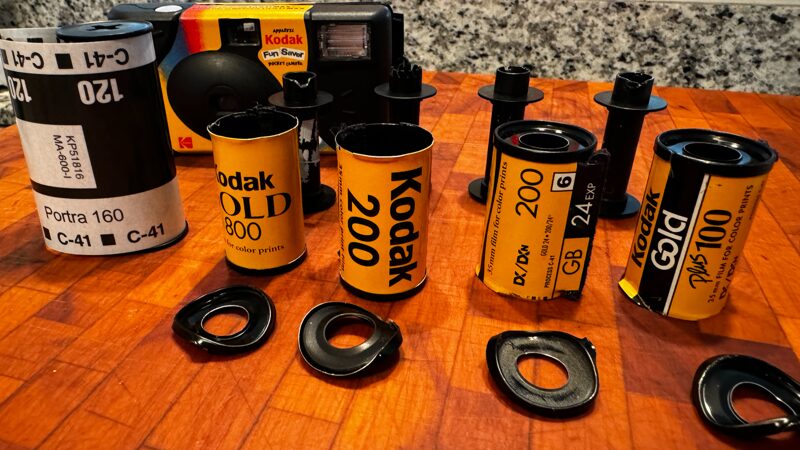 A row of five rolls of film on a wooden table, 4 35mm rolls, and one roll of 120, all Kodak