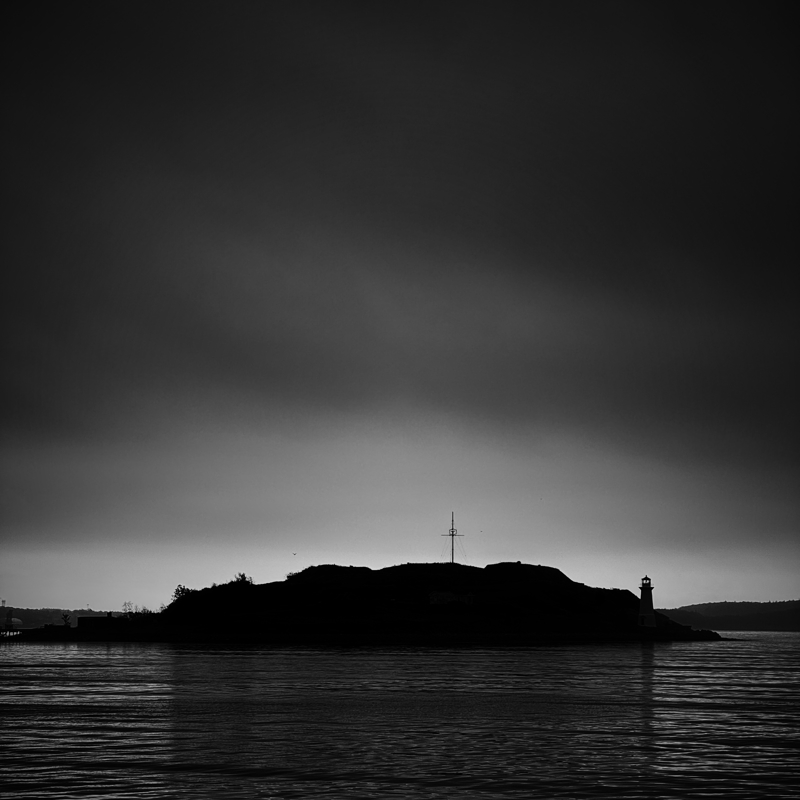 Georges Island glow A small island in shadow sits in calm water in front of a glow on the far horizon
