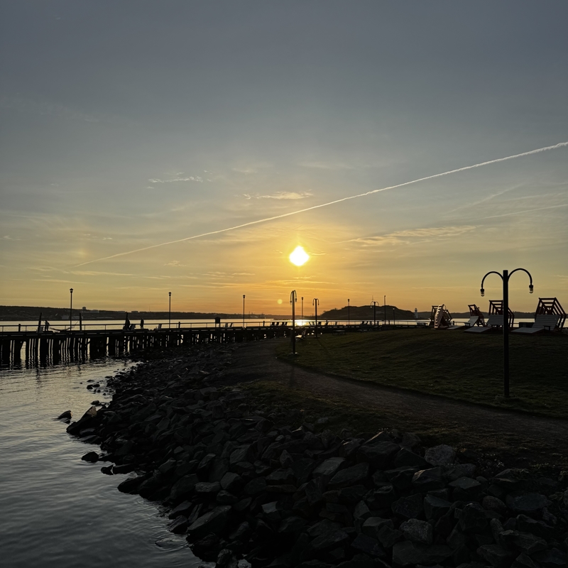 Good morning, Halifax A bright sun rises over calm harbour water, a small island and lighthouse is seen in the distance and a airplane trail streaks across the sky