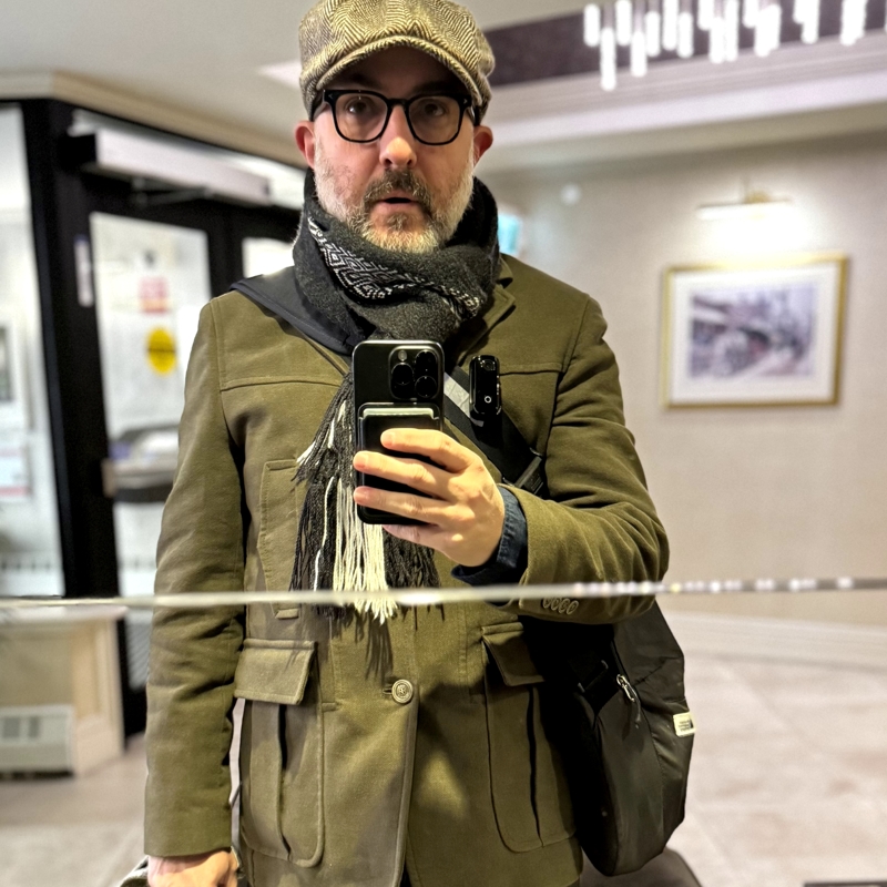 Milestones A middle-aged man appears in a mirror selfie wearing a dark green wool coat, black-and-white scarf and a newsboy cap