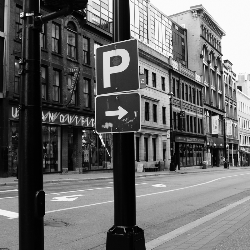 That way! A typical parking sign with a large, white P, and an arrow pointing left is attached to a light post. In small letters, the words that way are scribbled next to the arrow