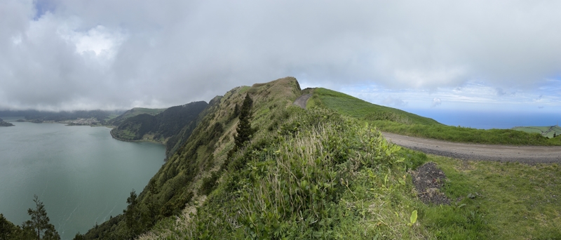 A hike along the rim A panoramic photo taken from a high vantage point on the rim of a volcano, a hiking trail is seen in the middle, the crater lake is seen in the left, the Atlantic Ocean on the right