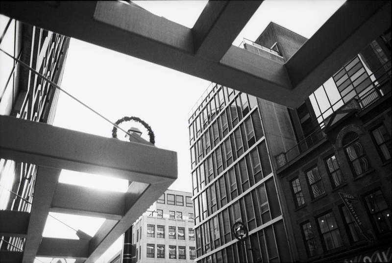 Looking up at buildings and an overhanging metal design feature creating a frame full of angles in every direction