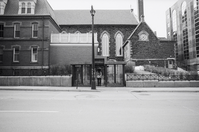 Gimme shelter A person looks down at their phone while standing in the door of a bus shelter, there is a large stone church in the background