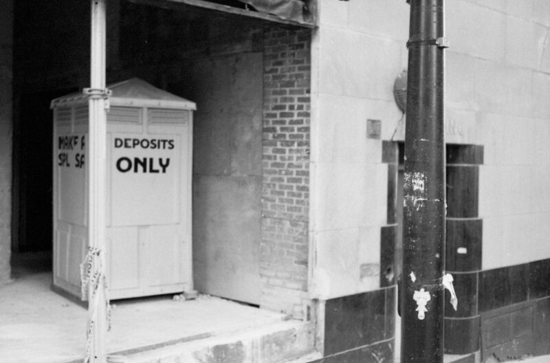 A construction toilet sits inside a building under construction. The words deposit only are stuck to the side in large black letters.