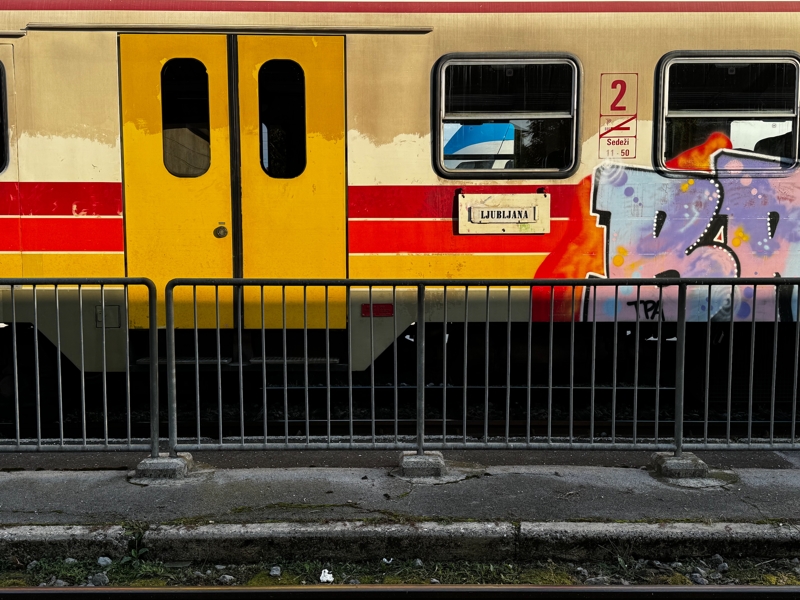 The side of a colourful, graffiti covered train car is lit up by the early morning sun, a small destination sign reading Ljubljana is posted next to the doors