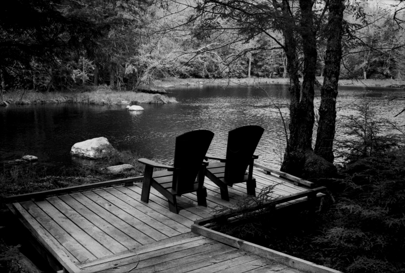 Mosquito buffet Two chairs sit next to each other on a wooden platform and boardwalk overlooking a gently rolling river. Trees overhang on all sides.