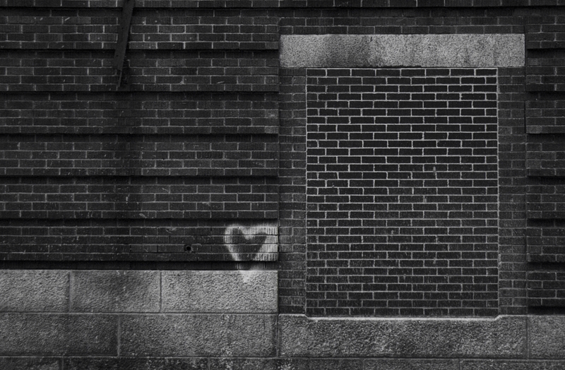 Signs of life A white heart is spray painted on a dark brick wall next to a large bricked-up window