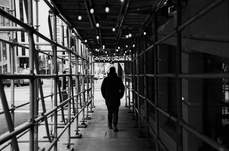 Street perspective Metal scaffolding is erected over a sidewalk as a pedestrian walks in shadow beneath it