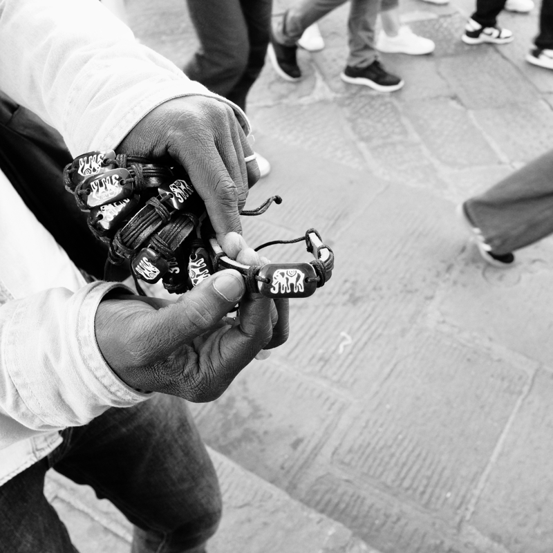 Senegalese street seller, Florence, September 2024 A man with dark skin holds bracelets in his hand against the background of the pavement