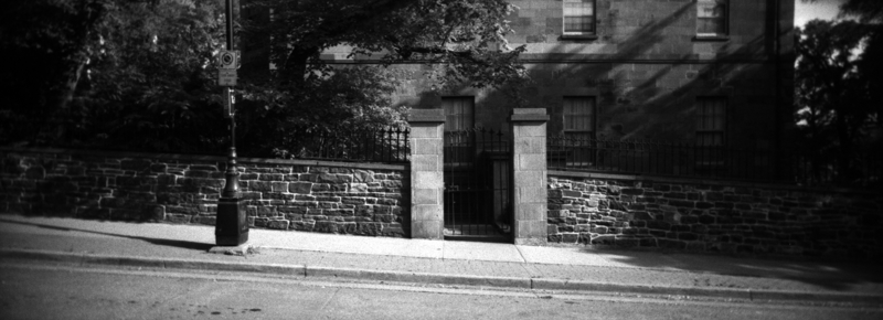 A wide panoramic view of stone wall with a stone gate in it with trees overhanging over the wall