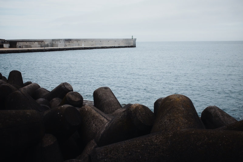 Farolim do Baía de Angra do Heroísmo, May 2025 A small green and white striped lighthouse stands alone at the end of a grey concrete seawall with dark concrete tetrapods in the foreground